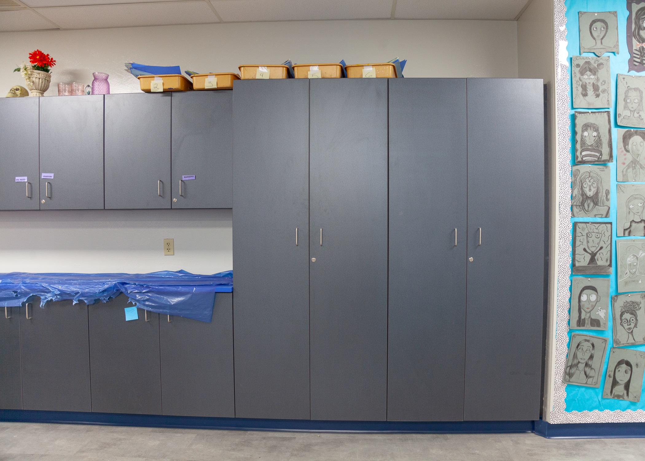 Art room with grey cabinets and a wall displaying kids drawings